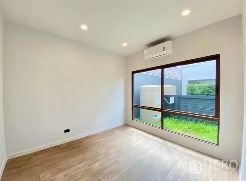 Detached House for sale in Bang Kapi, Bangkok - Ground-floor bedroom with large window to side garden and wall-mounted AC.