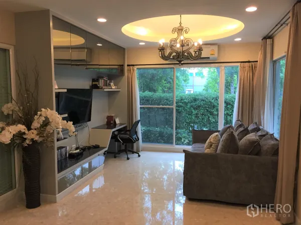 Detached House for sale in Saphan Sung, Bangkok - Bright TV room with built-in media wall, chandelier and large windows overlooking greenery.