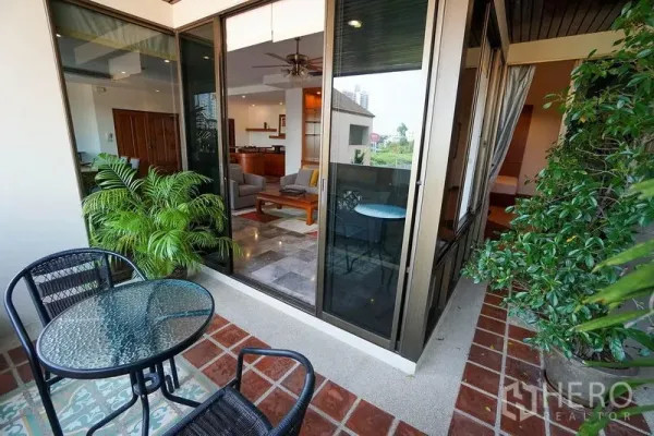 Apartment for rent in Watthana, Bangkok - Balcony with bistro table, plants and glass sliding doors to the living area.