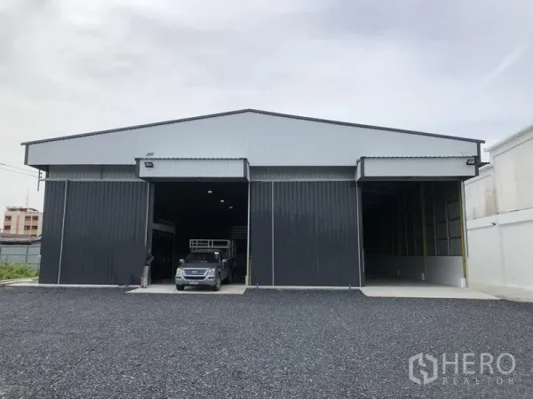 Warehouse for rent in Pathum Thani - Modern metal-clad warehouse exterior with two high roller doors and a gravel loading yard in Pathum Thani.