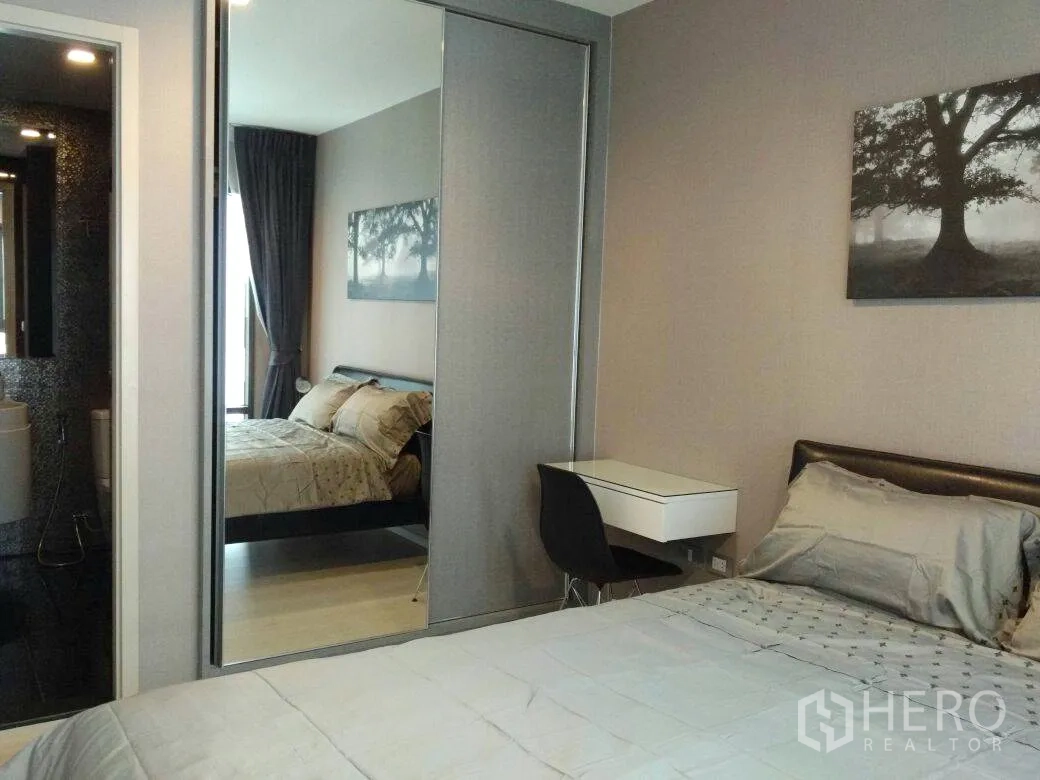 Condominium for rent in Khlong Toei, Bangkok - Bedroom in a modern Khlong Toei condo with mirrored wardrobe, desk, and view to a tiled bathroom.