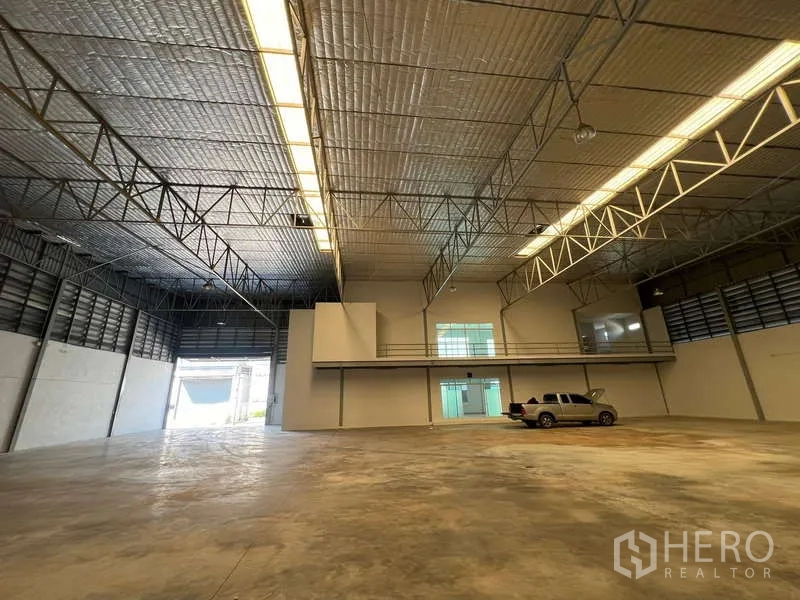 Warehouse for rent in Prawet, Bangkok - Wide warehouse interior showing skylight strips and a pickup on concrete floor.
