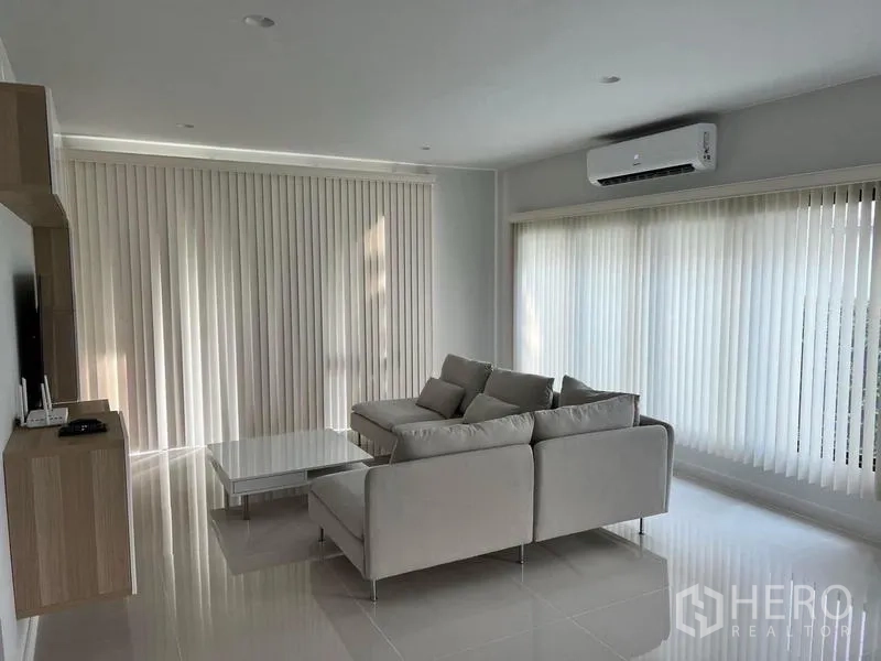 Detached House for rent in Bang Kapi, Bangkok - Minimalist living room with L-shaped sofa, large windows with vertical blinds and air conditioner.