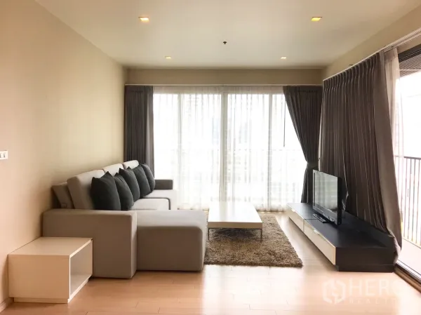 Condominium for rent in Watthana, Bangkok - Neutral-tone living room with L-shaped sofa, coffee table, TV console, and balcony-height glazing.