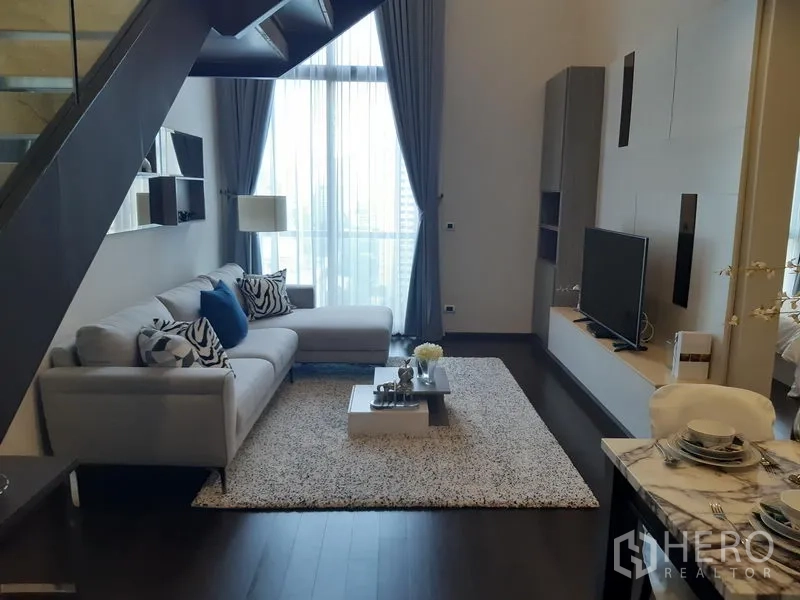Condominium for rent in Watthana, Bangkok - Modern living room with L-shaped sofa, TV wall, staircase and floor-to-ceiling windows.