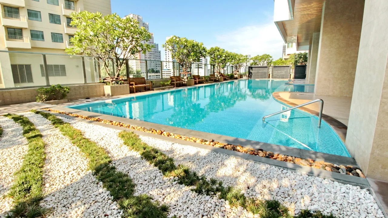 Condominium for rent in Khlong Toei, Bangkok - Rooftop swimming pool with sun loungers, trees and city skyline views.