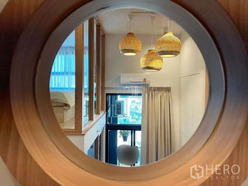 Condominium for rent in Huai Khwang, Bangkok - Circular wooden window framing a view of the living space with rattan pendant lights, curtains and air conditioner.