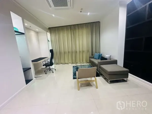 Condominium for rent or sale in Khlong Toei, Bangkok - Quiet home office with built-in desk, ergonomic chair and sectional sofa beside full-length curtains.