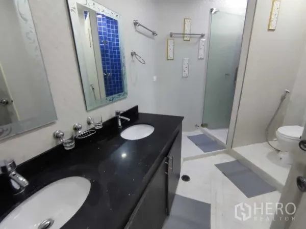 Condominium for rent in Khlong Toei, Bangkok - Modern bathroom with double vanity, glass-enclosed shower and toilet.