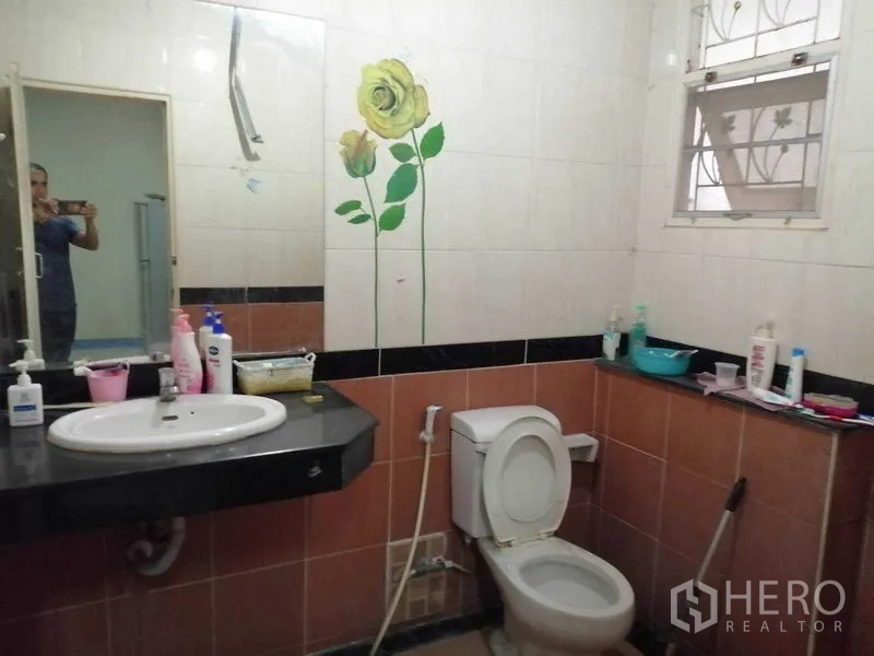 独立式住宅 出售在Prawet, Bangkok - 浴室铺砖，黑色台面洗手台与坐便器，墙面花卉装饰。