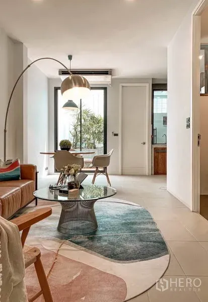 Townhouse for rent in Huai Khwang, Bangkok - Bright living and dining space with leather sofa, round glass coffee table and tall windows.