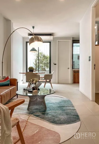 Townhouse for rent in Huai Khwang, Bangkok - Bright living and dining space with leather sofa, round glass coffee table and tall windows.
