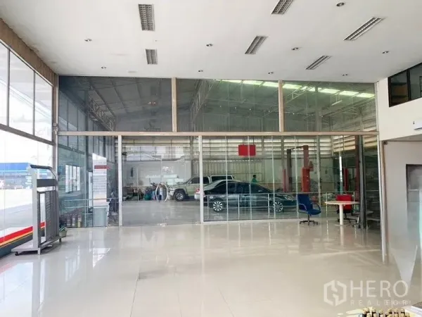 Warehouse for rent in Bang Khen, Bangkok - Glass-partitioned lobby opening to a rear workshop bay with vehicle service equipment and parked cars.
