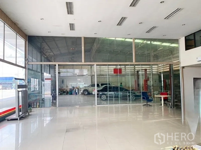 Warehouse for rent in Bang Khen, Bangkok - Glass-partitioned lobby opening to a rear workshop bay with vehicle service equipment and parked cars.
