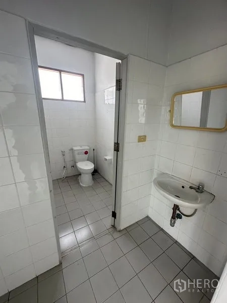 Factory for rent in Pathum Thani - Clean tiled restroom with toilet, sink, and window ventilation.