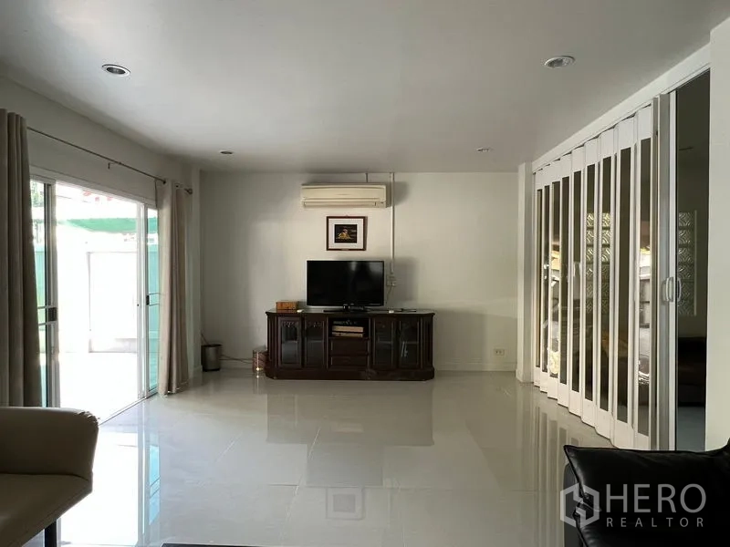 Detached House for rent in Bang Kapi, Bangkok - Living room with TV cabinet, sliding glass doors to patio and folding partition.