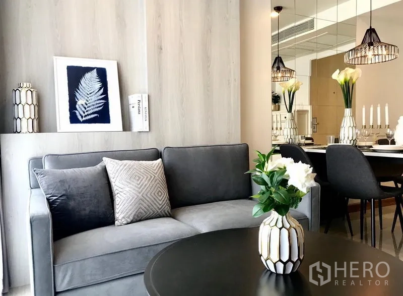 公寓 出租在Watthana, Bangkok - 现代客厅，灰色沙发、花瓶装饰，镜面墙与吊灯下的餐区相连。