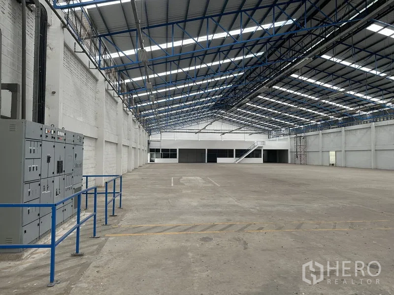 Factory for rent in Nonthaburi - Warehouse aisle with power panels, high roof and a staircase to office rooms.
