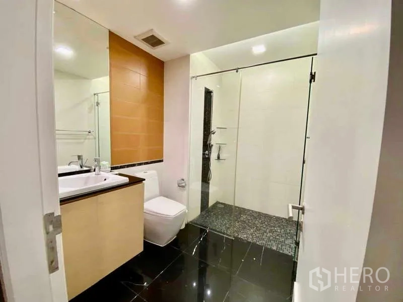 Condominium for rent or sale in Sathon, Bangkok - Guest bathroom with glass-enclosed shower, vanity, and black tile floor.