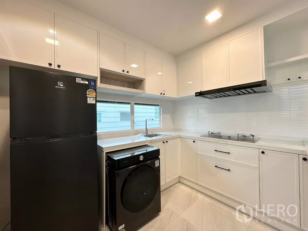 Detached House for rent in Bang Phli, Samut Prakan - White fitted kitchen with gas hobs, range hood and serving window counter.
