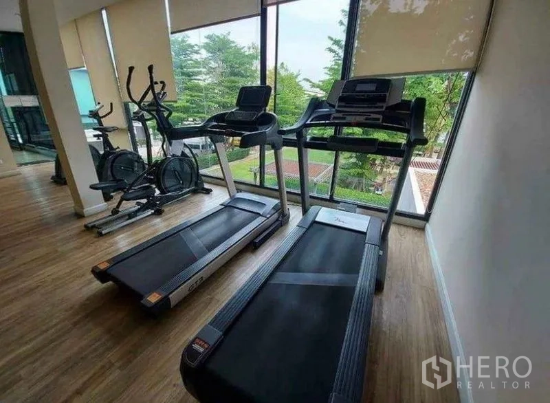 Townhouse for rent in Bang Phli, Samut Prakan - Fitness room with treadmills and exercise bikes facing full-height windows and greenery.