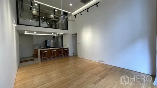公寓 出租在Watthana, Bangkok - 挑高客厅带夹层与玻璃隔断，轨道灯与开放式厨房中岛吧台，浅色木地板