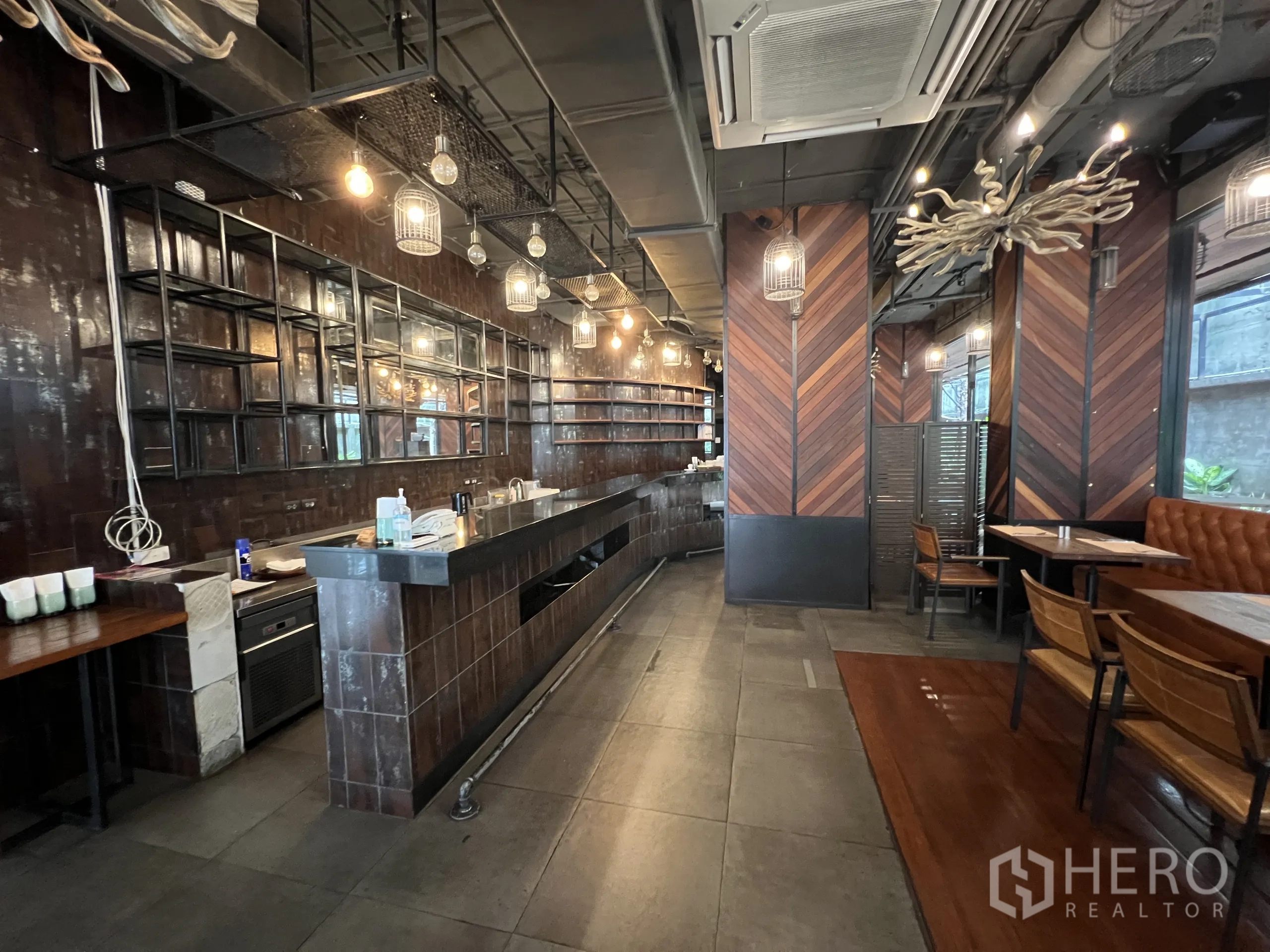 Retail Space for rent in Watthana, Bangkok - Long service bar with open shelving, industrial ceiling, pendant cage lights, and booth seating.