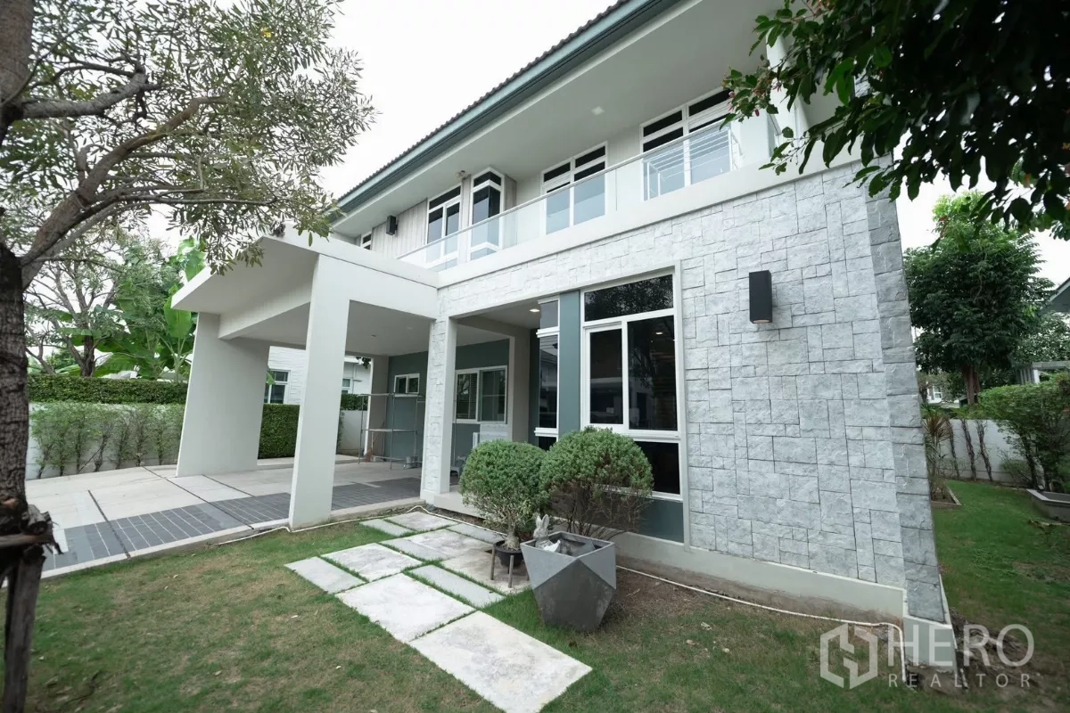 Detached House for rent or sale in Prawet, Bangkok - Front corner showing stone-clad exterior wall, large windows and a small lawn.