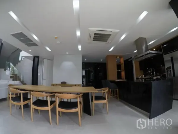 Apartment for rent in Khlong Toei, Bangkok - Sleek kitchen with a black island, built-in appliances, and an adjacent dining table under recessed lighting.