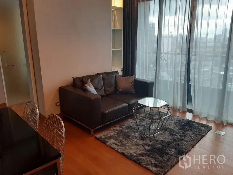 Condominium for rent in Khlong Toei, Bangkok - Living area with geometric coffee table and sheer curtains opening to skyline views.