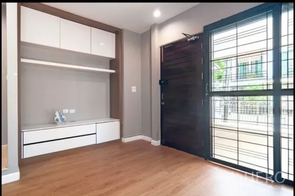 Townhouse for sale in Khlong Toei, Bangkok - Built-in media cabinet beside a solid wood entry door, with wood floors and sliding window.