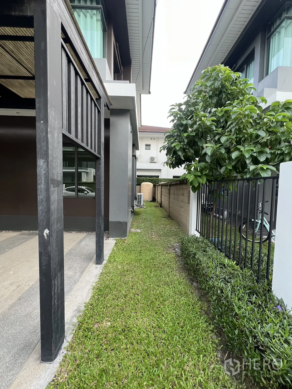 Detached House for rent in Bang Kapi, Bangkok - Narrow side garden with a grass path along the fence and a tree.