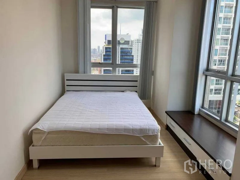Condominium for rent in Bang Rak, Bangkok - Secondary bedroom with corner windows, white bedframe and built-in bench storage.