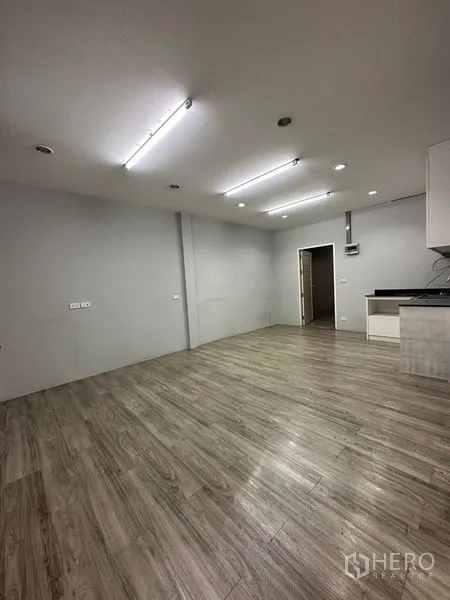 零售空间 出租在Khlong Toei, Bangkok - 开放式零售区，灰色墙面、木纹地面、顶灯，以及通往后勤区的门。