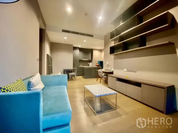 公寓 出租或出售在Bang Rak, Bangkok - 客厅设墙面层架、电视柜、蓝色沙发与茶几，通向厨房。