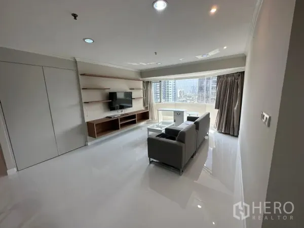 Condominium for rent in Watthana, Bangkok - Bright living room with sofa set, TV wall and shelving, plus a wide bay window overlooking Bangkok’s skyline.