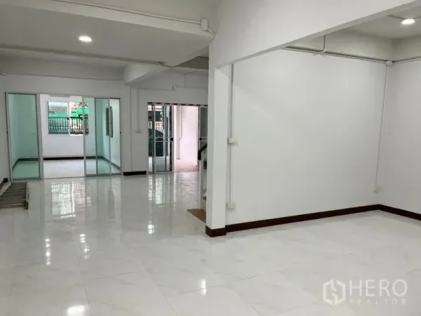 Townhouse for rent in Din Daeng, Bangkok - Bright open-plan living area with glossy white floor tiles and sliding glass doors to separate rooms.