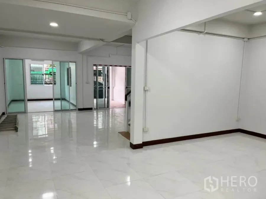 Townhouse for rent in Din Daeng, Bangkok - Bright open-plan living area with glossy white floor tiles and sliding glass doors to separate rooms.