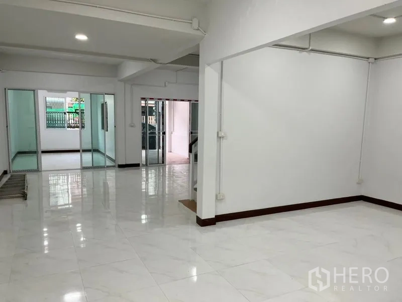 Townhouse for rent in Din Daeng, Bangkok - Bright open-plan living area with glossy white floor tiles and sliding glass doors to separate rooms.