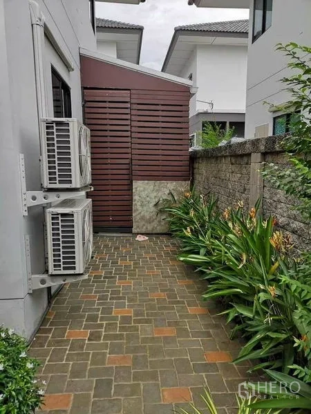 บ้าน ขายในBang Phli, Samut Prakan - ทางเดินด้านข้างปูอิฐบล็อก มีคอมเพรสเซอร์แอร์และต้นไม้ริมกำแพง