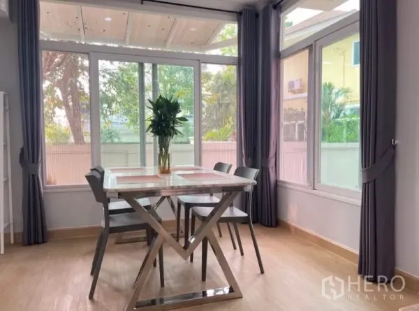 Detached House for rent or sale in Lat Phrao, Bangkok - Corner dining space with floor-to-ceiling windows, curtains and a marble-top table.