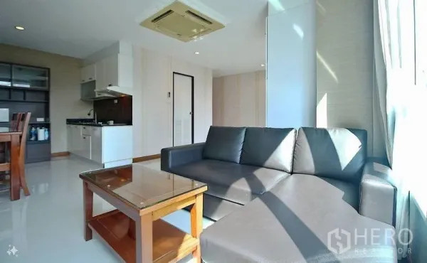 公寓 出售在Watthana, Bangkok - 采光充足的起居区，L型皮沙发、茶几，开放式厨房与吊顶空调。