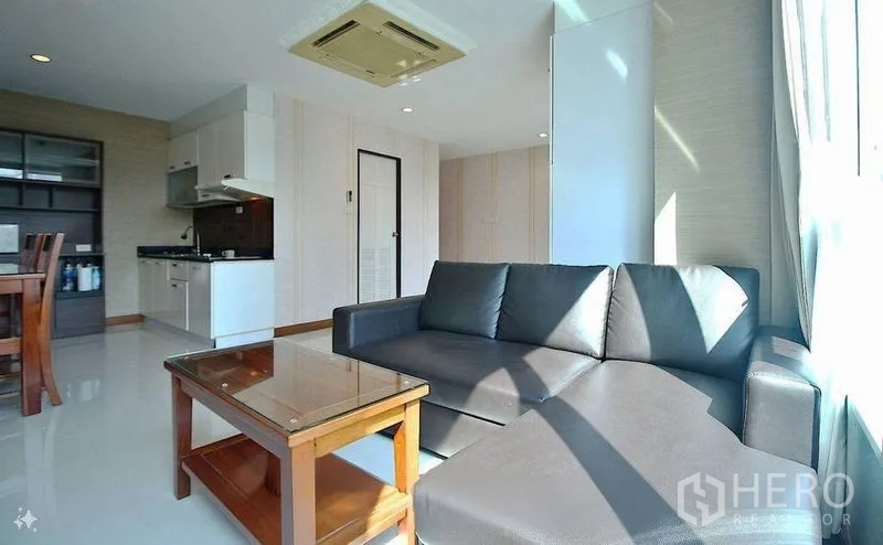 公寓 出售在Watthana, Bangkok - 采光充足的起居区，L型皮沙发、茶几，开放式厨房与吊顶空调。