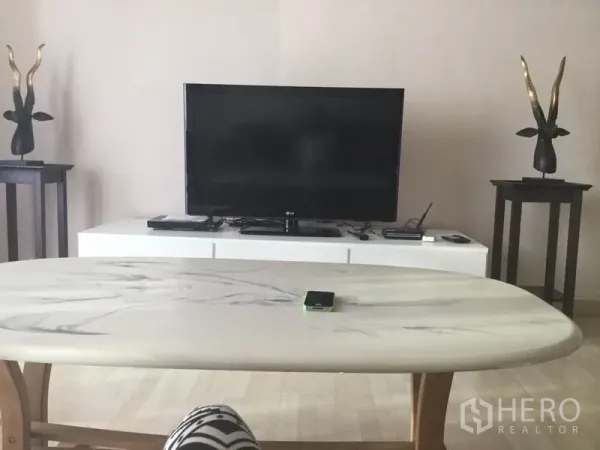 公寓 出租在Watthana, Bangkok - 客厅电视墙，平板电视置于白色电视柜上，搭配大理石面茶几与装饰摆件。