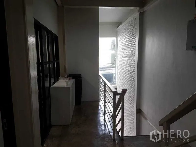Shophouse for sale in Bang Rak, Bangkok - Upper landing with metal railing and light from a glass-block wall near the stairs.
