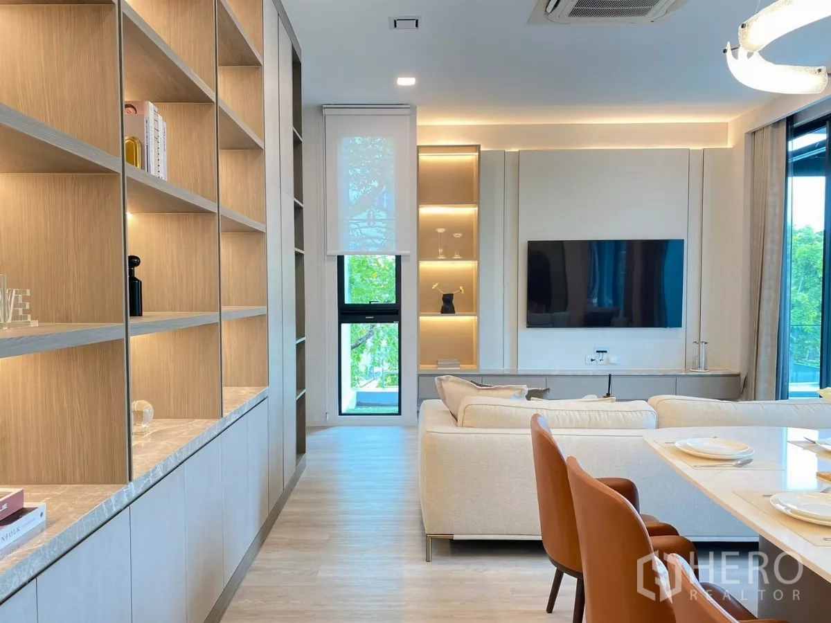 Detached House for rent in Saphan Sung, Bangkok - Living area featuring wall‑length wood shelving, a TV feature wall, dining table, and large windows with warm lighting.