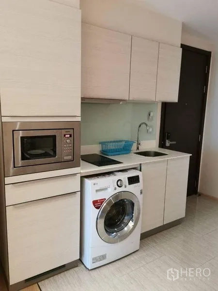 Condominium for rent or sale in Watthana, Bangkok - Compact modern kitchen with cabinets, sink, cooktop, microwave and front-load washer.