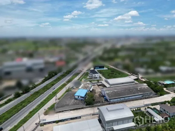 ที่ดิน ขายในBang Bua Thong, Nonthaburi - ภาพมุมสูงเห็นถนนสายหลักในพื้นที่ อาคารโรงงานหลังคาสีน้ำเงิน และทางเชื่อมรอบชนบท
