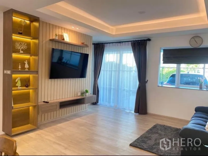 Townhouse for rent in Prawet, Bangkok - Living room with wall-mounted TV, illuminated shelves and floor-to-ceiling balcony doors.