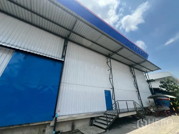 货栈 出租在Lat Krabang, Bangkok - 带遮棚的装卸区，配大型蓝色滑门和通往月台的楼梯。